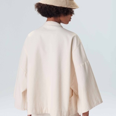 Pessoa de costas com chapéu bege e roupa creme de manga larga