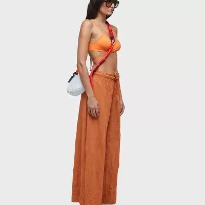 Mulher com top alças laranja, calças largas castanhas e bolsa branca com correia vermelha