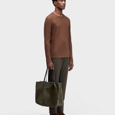 Homem com camisola castanha de manga comprida, calças castanhas, sapatos castanhos e mala verde com alças pretas.