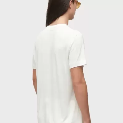 Pessoa de costas com t-shirt branca, calças brancas e óculos de armação amarela num fundo cinza claro.