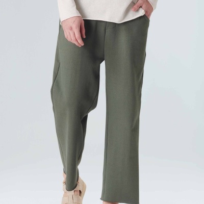 Calças verdes largas com blusa bege e sandálias bege em fundo branco.