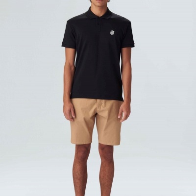 Homem com polo preta, calções bege e ténis pretos em fundo branco