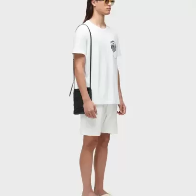 Homem com t-shirt branca e calções, mala preta e óculos de sol castanhos