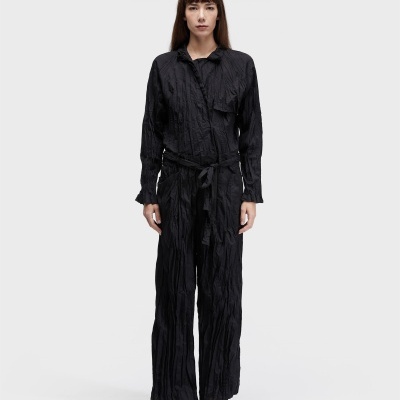 Macacão preto feminino texturizado com cinto e sandálias brancas.