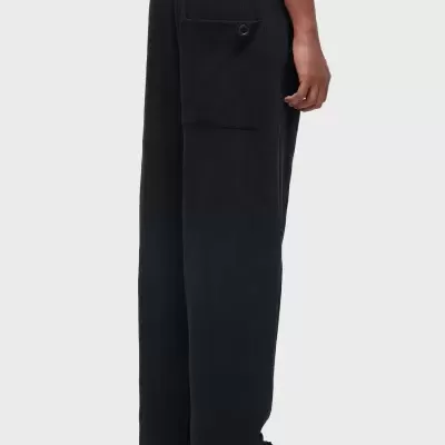 Calças pretas texturizadas com bolso traseiro e botão em fundo cinza.