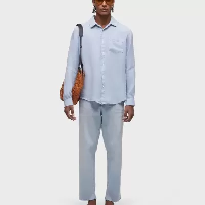 Homem com roupa azul claro, óculos de sol, sandálias castanhas e bolsa castanha.