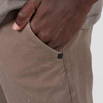 Calças castanhas com bolso lateral e selo preto numa mão.