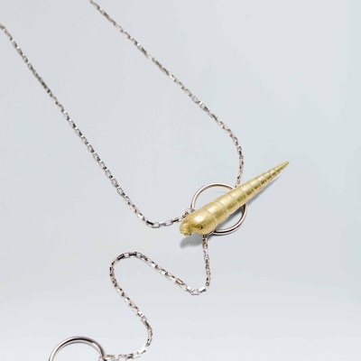 Colar com pendente cone dourado e corrente prateada sobre fundo cinzento