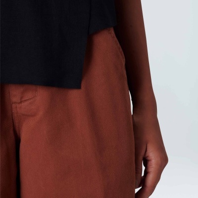 Detalhe de calças castanhas largas com peça preta e mão ao lado