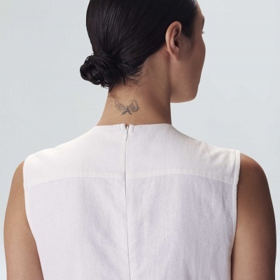 Vestido branco sem mangas com fecho invisível nas costas, cabelo preso e tatuagem na nuca