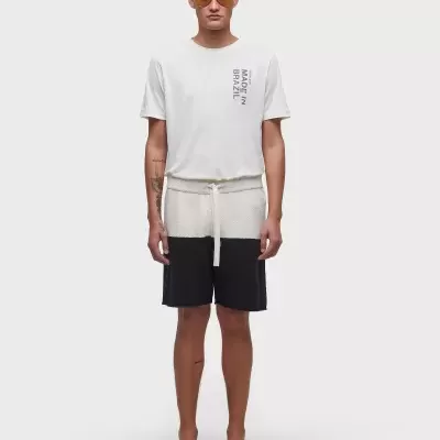 Homem com t-shirt branca, calções bege e pretos, chinelos pretos e óculos de sol