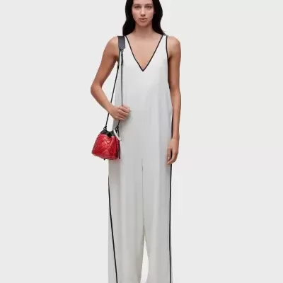 Modelo feminina com macacão branco com detalhes pretos e bolsa vermelha