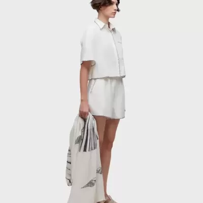 Modelo com camisa branca de manga curta, calções brancos, sandálias e cachecol com padrão de conchas