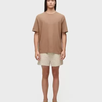 Modelo a usar t-shirt castanha, calções brancos com padrão e mocassins castanhos.