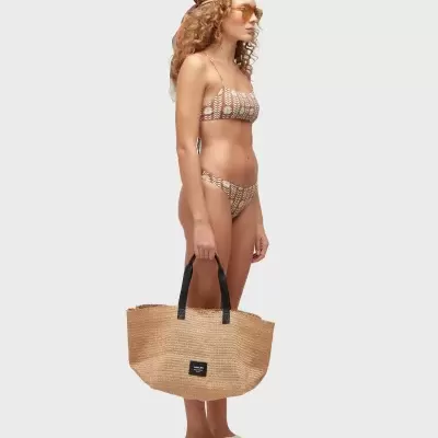 mulher de perfil com biquíni bege padrão geométrico, bolsa de palha, lenço na cabeça, óculos de sol e sandálias