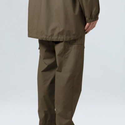 Homem vestido com calças e blusão verde-oliva e ténis pretos e verdes num fundo cinzento claro.