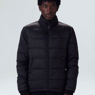 Homem a usar casaco preto acolchoado com fecho e bolsos num fundo cinza claro.