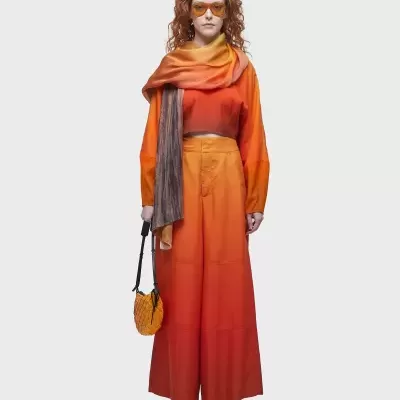 Mulher vestida com conjunto laranja e vermelho, cachecol e óculos de sol laranja, bolsa amarela pequena