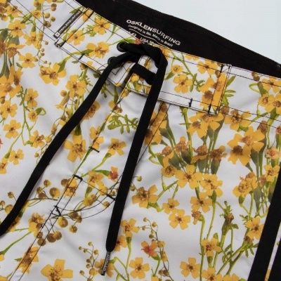 Calções de banho brancos com flores amarelas e verde e cordão preto para ajuste.