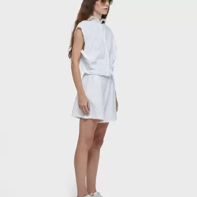 Mulher vestindo conjunto branco de camisa sem mangas e saia, sapatilhas brancas e óculos amarelos