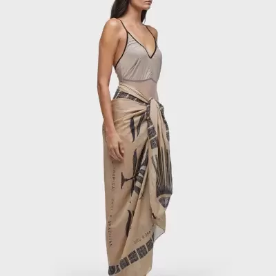 Mulher com body cinzento, saia pareô bege estampada, ténis brancos e óculos escuros