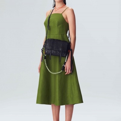 Mulher com vestido verde midi, sandálias castanhas e bolsa preta com alça de corrente