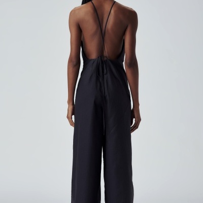 Macacão preto de costas com alças finas cruzadas em fundo branco.