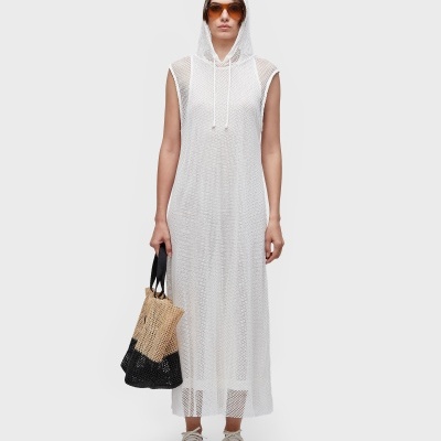 Mulher com vestido branco de malha e capuz, ténis brancos, óculos escuros e saco bicolor em malha