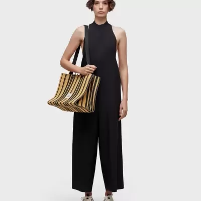 Mala tote às riscas castanhas e pretas em modelo com macacão preto.