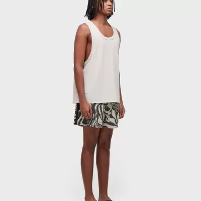 Homem com colete branco, calções com padrão preto e bege e sandálias pretas