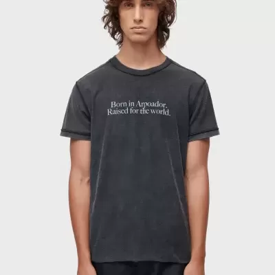 Homem com t-shirt preta com texto 'Born in Arpoador. Raised for the world.' e calções pretos