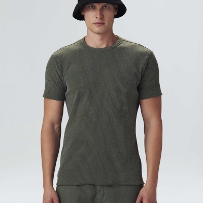 Homem com t-shirt verde musgo e chapéu preto em fundo neutro