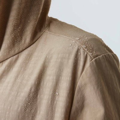 Peça de vestuário bege com capuz e gotas de água na superfície