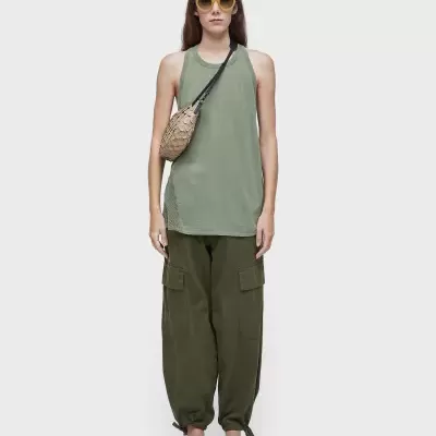 Mulher vestindo top verde claro, calças cargo verdes escuras, sandálias pretas, óculos de sol amarelos e bolsa bege com alça preta.