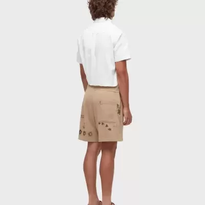 Homem com camisa branca e calções castanhos com estampados de estrelas e sol vistos de costas.