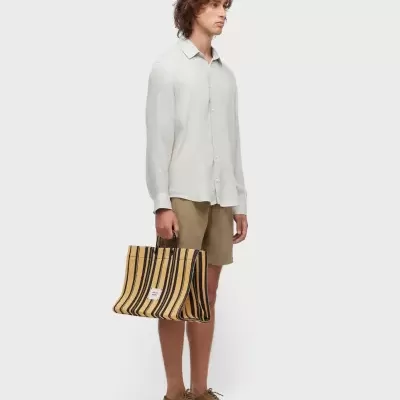 Homem de camisa branca, calções bege e bolsa listrada amarela e preta em fundo branco