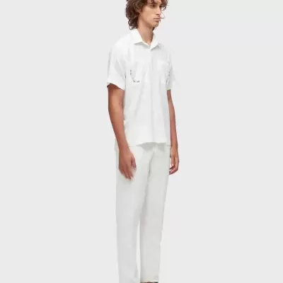 Homem de camisa branca de manga curta com bordados e calças brancas com sandálias pretas