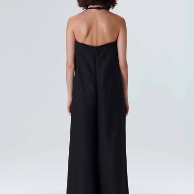 Modelo de costas vestindo vestido preto comprido sem mangas com alças no pescoço em fundo cinza claro