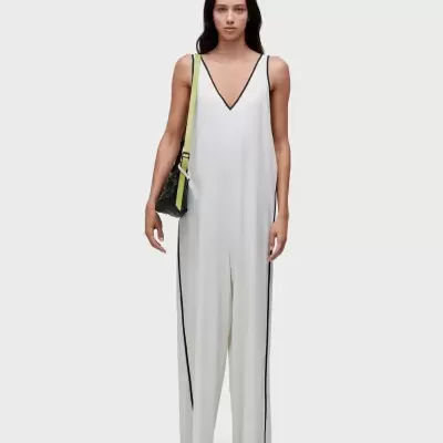 Modelo com macacão branco de corte largo e mala preta com alça amarela