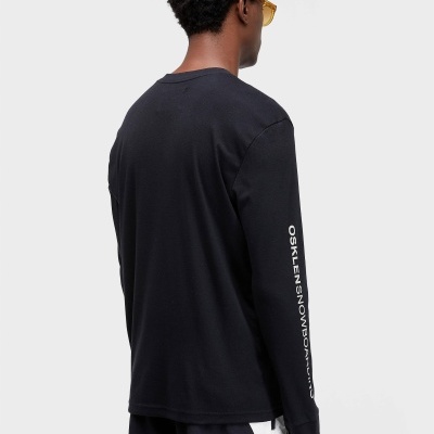 Camisola preta de manga comprida com texto na manga usada por homem com óculos amarelos.
