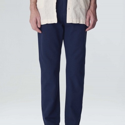 Calças azuis escuras de tecido com corte recto, parte inferior do corpo de um homem vestindo camisa bege e sandálias pretas.