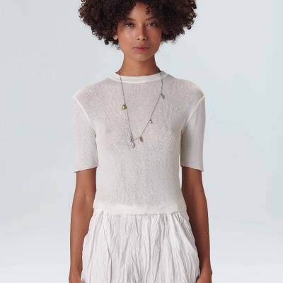 Mulher com camisola branca de manga curta e calças brancas, em fundo claro