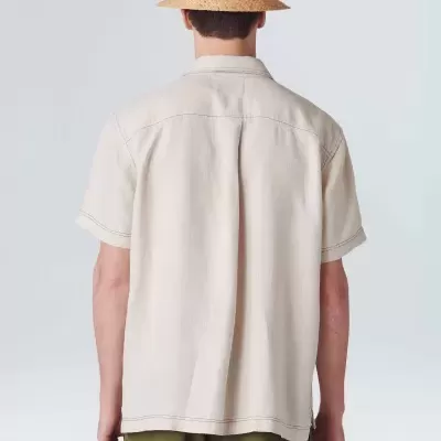 Homem de costas com camisa bege, chapéu de palha e calções verdes com padrão