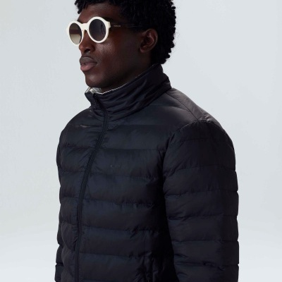 Homem a usar casaco acolchoado preto e óculos de sol brancos.