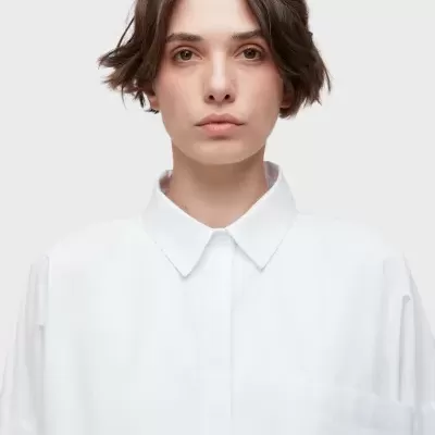 Camisa branca de algodão com gola clássica e bolso à esquerda, em fundo cinza claro