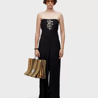 Mulher com macacão preto bordado, óculos de sol e mala listrada