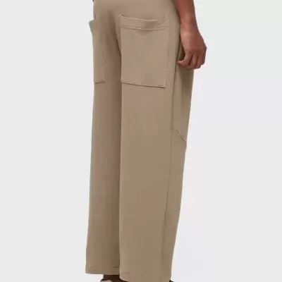 Calças largas bege com dois bolsos traseiros e sapatilhas desportivas pretas.