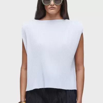 Mulher com top branco canelado, calças pretas largas e óculos de sol verdes