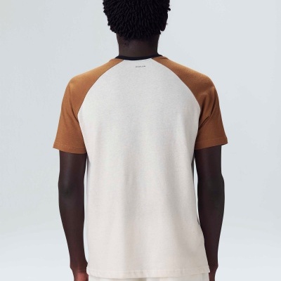 Homem de costas com t-shirt branca e castanho alaranjado e calças brancas