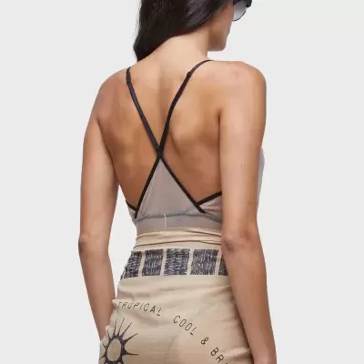 Mulher de costas com top transparente e saia estampada bege em fundo cinza claro